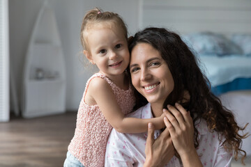 Happy beautiful mom and cute little girl home portrait. Positive cheerful mother and daughter kid hugging on floor, looking at camera, smiling, posing, expressing love, tenderness