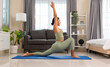 Healthy woman in green top and leggings doing yoga in Low Lunge pose or Anjaneyasana on blue mat in bedroom at home..