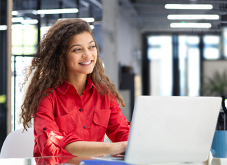 attractive cheerful business woman in red shirt working on laptop at modern office.