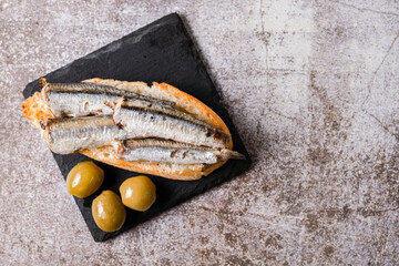 tapa of sardines on a slice of bread with tomato and olives on a white plate with a typical spanish white background