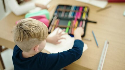 Sticker - Adorable caucasian boy student drawing on notebook sitting on table at classroom