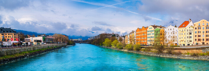  Innsbruck city skyline on a April day with vibrant colorful houses, the snowy Alps mountains, foggy cloudscape, the green Inn River in historic landmark town of Tyrol in western Austria