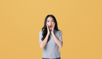 Wall Mural - Young Asian doing a shocked surprise gesture with her hands on her face isolated yellow color background