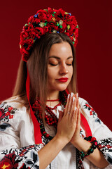 Wall Mural - Portrait of ukrainian woman in traditional ethnic clothing and floral red wreath on viva magenta studio background. Ukrainian national embroidered dress call vyshyvanka. Pray for Ukraine