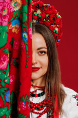 Wall Mural - Portrait of ukrainian woman in traditional ethnic clothing and floral red wreath with handkerchief on viva magenta studio background. Ukrainian national embroidered dress call vyshyvanka