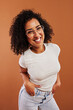 © Flamingo Images - Young woman smiling with her hands in her pockets on an orange background