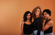 © Flamingo Images - Diverse women in black tops and jeans standing against an orange background