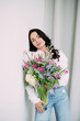 © Stanislav - Young happy woman standing and holding vase with flowers bouquet in her hands.