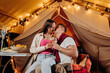 © bondvit - Happy lovely couple relaxing in glamping on summer evening and drinking wine near cozy bonfire. Luxury camping tent for outdoor recreation and recreation. Lifestyle concept
