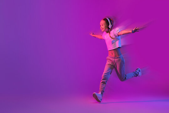 Wall Mural - Carefree preteen girl with wireless headphones running towards copy space