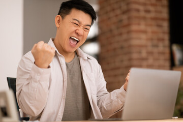 Wall Mural - Overjoyed asian man using laptop and shaking fists, celebrating great online news and success, working from home