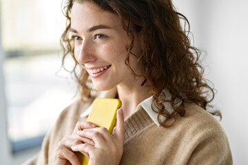 Smiling pretty curly young woman model using mobile phone, happy girl holding smartphone browsing internet on cellphone technology device standing isolated on white background, close up view.