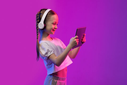Wall Mural - Happy school-age blonde girl using tablet and headphones, copy space