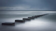 Long exposure of cement blocks holding down a drain pipe reaching out into the ocean on a stormy day