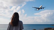 © AdriFerrer - Young woman looking at plane flying above the sea. Generative AI
