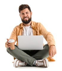 Young bearded man with cup of coffee and laptop sitting on white background