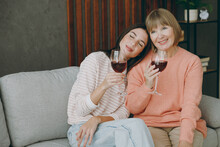 Two Calm Adult Women Mature Mom Young Kid Wear Casual Clothes Drink Wine Put Head On Shoulder Sit On Gray Sofa Couch Stay At Home Flat Rest Relax Spend Free Spare Time In Living Room. Family Concept.