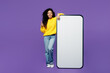 © ViDi Studio - Full body happy fun young woman of African American ethnicity wear casual yellow sweater big huge blank screen mobile cell phone smartphone with area show thumb up isolated on plain purple background.