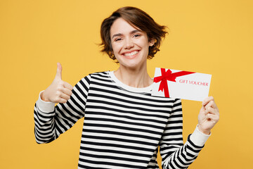 Wall Mural - Young woman wears casual striped black and white shirt hold gift certificate coupon voucher card for store show thumb up isolated on plain yellow color background studio portrait. Lifestyle concept.