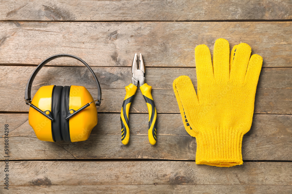 Pliers, hearing protectors and gloves on wooden background