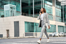 Full body portrait of successful African American business woman having phone call outdoor. Middle age businesswoman in suit talking on smartphone, walking city urban street at business office center.