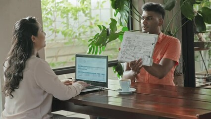 Wall Mural - medium shot of indian man discussing business plan on paper with female colleague as she using lapto