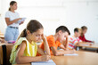 © JackF - Portrait of interested diligent preteen schoolgirl sitting at school desk and writing exercises at lessons with classmates