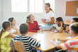 © JackF - Kids sitting around desk in classroom and studying during lesson. Teacher explaining subject to pupils.