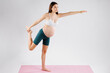 Portrait of dark haired pregnant woman doing aerobics in sports studio on pink yoga mat. Lateral vision. Healthy sport