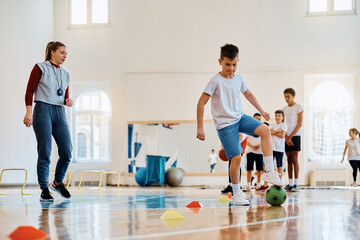 Elementary student practicing with soccer ball during physical education class at school gym.