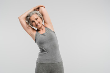 cheerful grandmother in sportswear exercising and smiling isolated on grey.