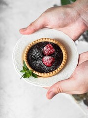 Poster - Closeup of a tart with chocolate and berries, served on a vintage ceramic plate in a woman's hands