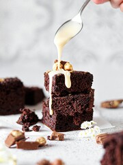 Poster - Closeup of a person pouring white chocolate cream over chocolate brownies, on a bright background