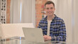 © stockbakers - Young Casual Man Smiling at Camera while Working on Laptop