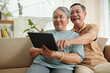 © DragonImages - Happy aged couple waching comedy movie on digital tablet