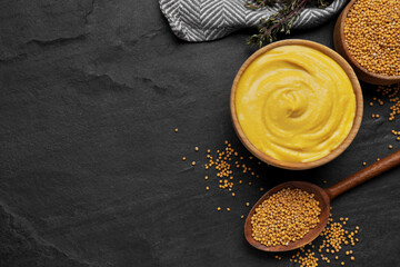 Bowl with delicious mustard and seeds on black textured table, flat lay. Space for text