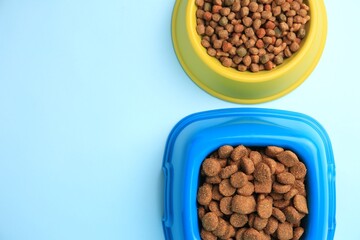 Wall Mural - Dry pet food in feeding bowls on light blue background, flat lay. Space for text