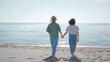 © olezzo - Young lesbian couple walking barefoot along the seashore holding hands. Love LGBT concept