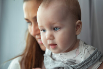 Wall Mural - Adorable newborn baby on hands loving happy mom at home, looking away. Mother with kid together in living room. Mom care 6 months old infant child. Concept of motherhood, maternity. Copy ad text space