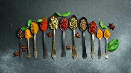 Wall Mural - A set of colored spices in metal spoons. On a black slate background. Top view.