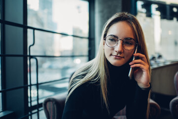 Young female talking on smartphone while sitting in cafe