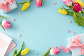 Mother's Day celebration idea. Flat lay composition of gift boxes with bows postcard with hearts and pink tulips flowers on isolated pastel blue background with blank space in the middle