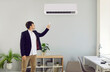 © Studio Romantic - Businessman turns on the AC system in a modern office workplace interior. Young man who works in the office switches on the air conditioner to have cool, fresh air flow during summer heat