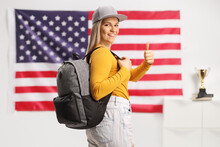 Female Student With A Backpack Showing Thumbs Up In Front Of USA Flag