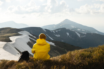 Wall Mural - A tourist sits on the edge of a mountain peak. Sunny mountains with snow on the background. Landscape photography