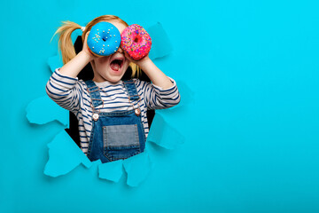 Happy cute girl is having fun played with donuts on black background wall. Bright photo of a child. 