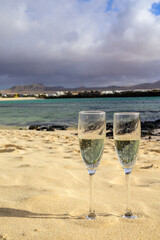 Two glasses of white champagne or cava sparkling wine served on white sandy tropical beach and blue ocean, romantic vacation, winter sun on Fuerteventura, Canary, Spain