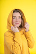© Татьяна Волкова - Portrait of attractive 40-year-old woman in yellow hoodie with hood on her head on yellow background in studio.