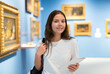 Portrait of a positive girl visitor with an information booklet attending an exhibition of paintings in an art gallery