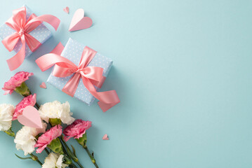 Wall Mural - Mother's Day concept. Top view flat lay photo of gift boxes with pink ribbons, carnation flowers, and pink paper hearts on pastel blue background with empty space for text or advert